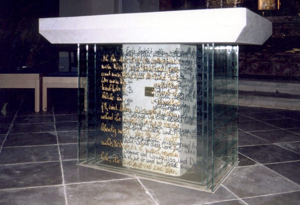 Altar mit dicker weißer Marmorplatte und einen gemauerten Fuß. Umgeben mit beschriebenen Glasplatten in Gold und schwarz