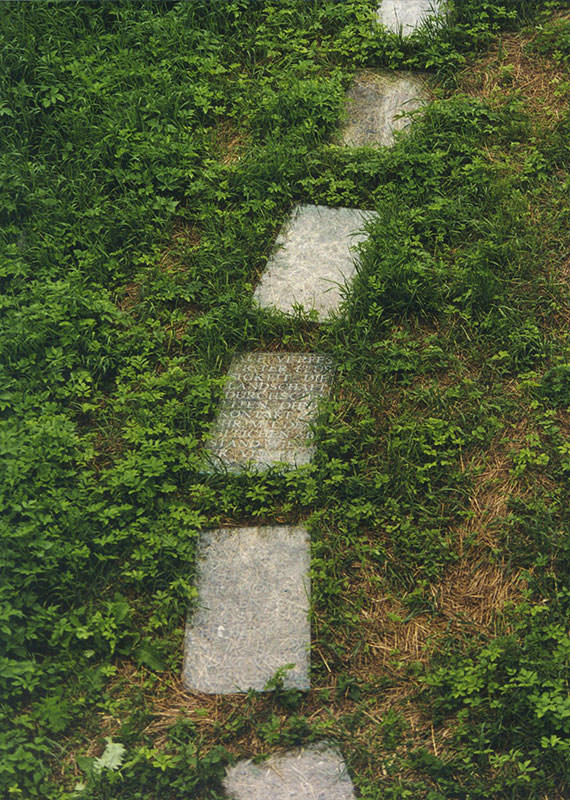 Glasplatten mit eingravierter Schrift liegen in Form eines Weges auf einem Grasbedecktem Boden