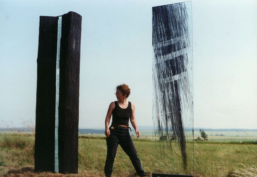Frau steht zwischen hohen Stelen auf einem Feld