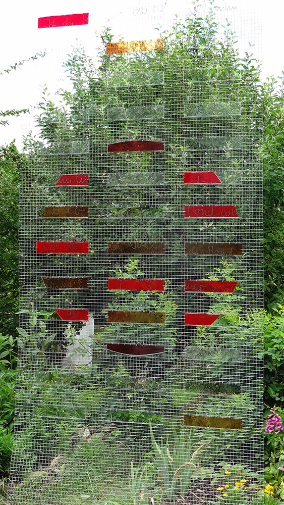 Drahtgeflecht mit roten Glasplatten vor Blätterhintergrund